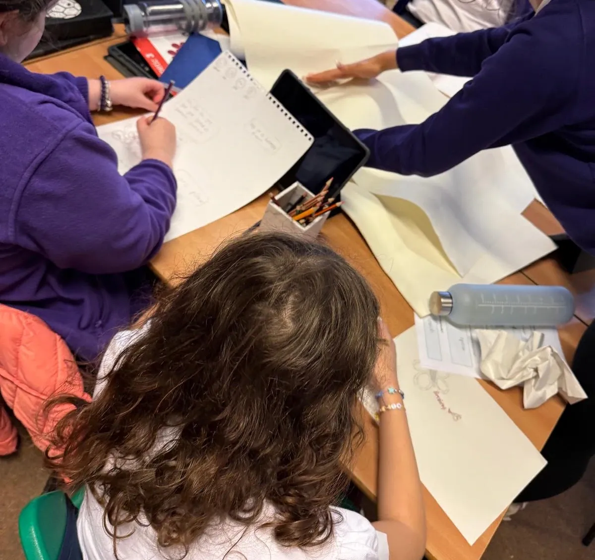 Several participants sitting around a table, creating several drawings on large sheets of paper