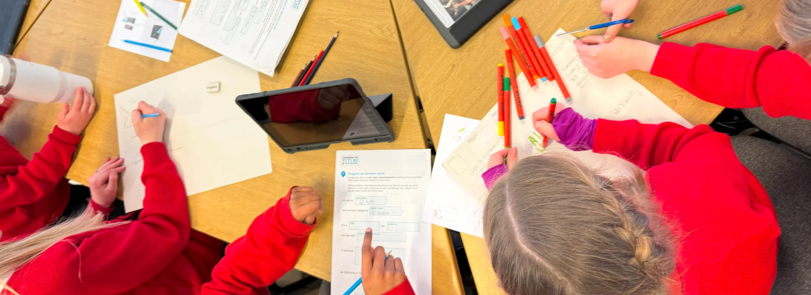 Four participants sitting around a table, photographed from above, creating drawings and filling out worksheets