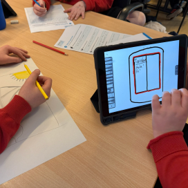 Three children sitting around a table, one drawing a translation app on a tablet, another drawing it on paper, and the third is filling out a worksheet